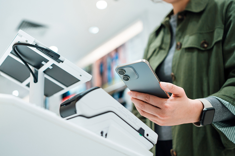 A customer holds a smartphone near a point-of-sale terminal in a store.